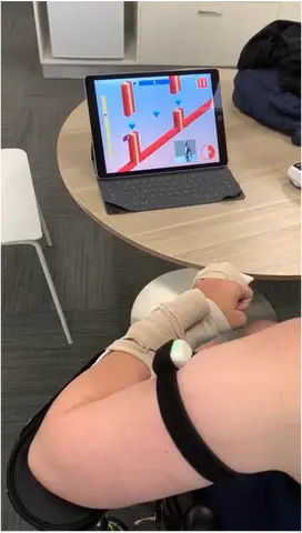 A LusioMATE sensor strapped to the forearm while playing a game on a tablet propped on a table